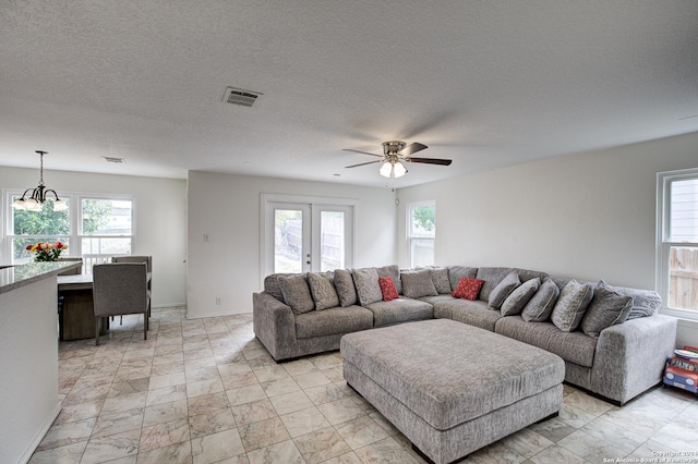 living room with a textured ceiling, french doors, and ceiling fan with notable chandelier