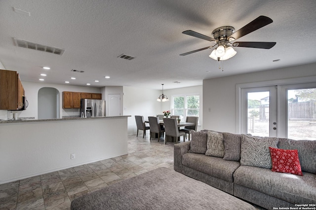 living room featuring a textured ceiling, french doors, and ceiling fan with notable chandelier