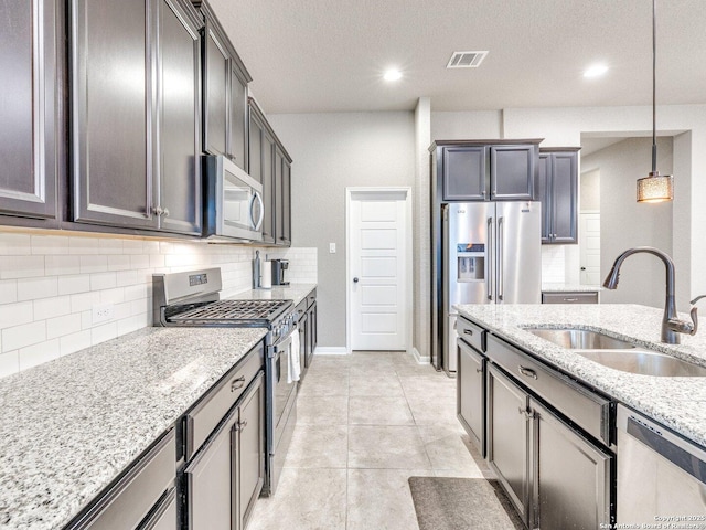 kitchen with light stone countertops, appliances with stainless steel finishes, sink, light tile patterned floors, and pendant lighting