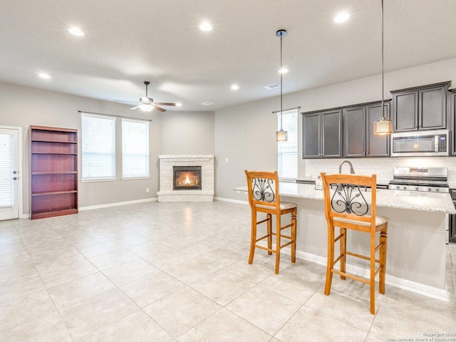 kitchen with appliances with stainless steel finishes, backsplash, light stone counters, hanging light fixtures, and a breakfast bar area