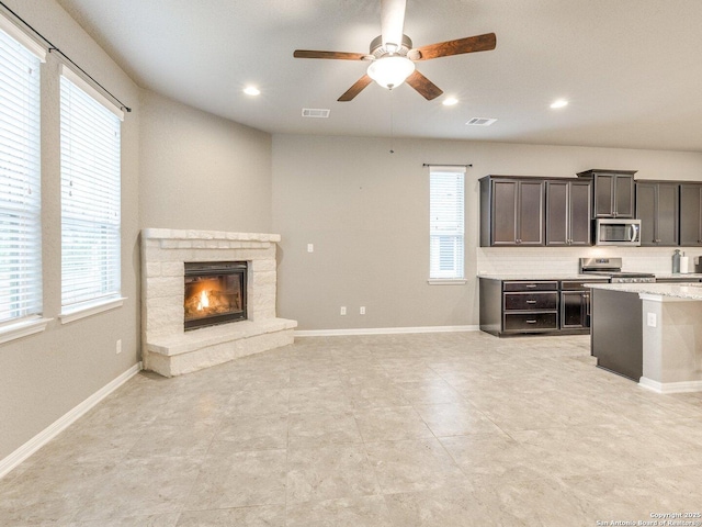 interior space with dark brown cabinetry, stainless steel appliances, a stone fireplace, plenty of natural light, and decorative backsplash