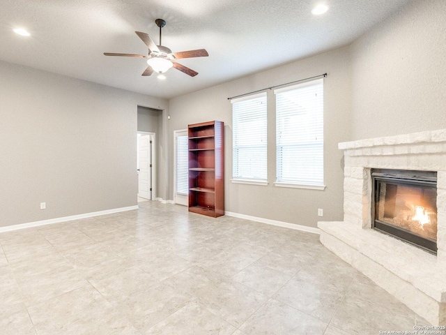 unfurnished living room featuring a stone fireplace and ceiling fan