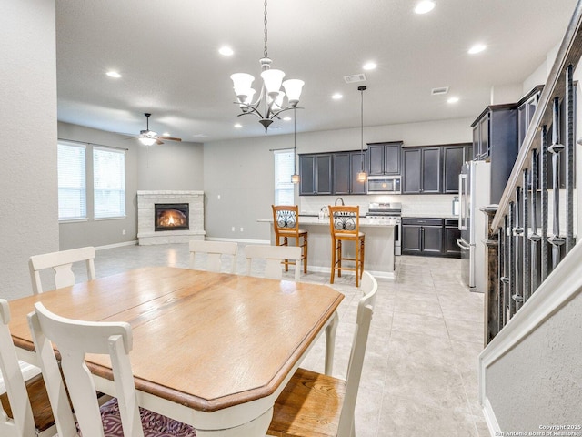 tiled dining area featuring a fireplace and ceiling fan with notable chandelier