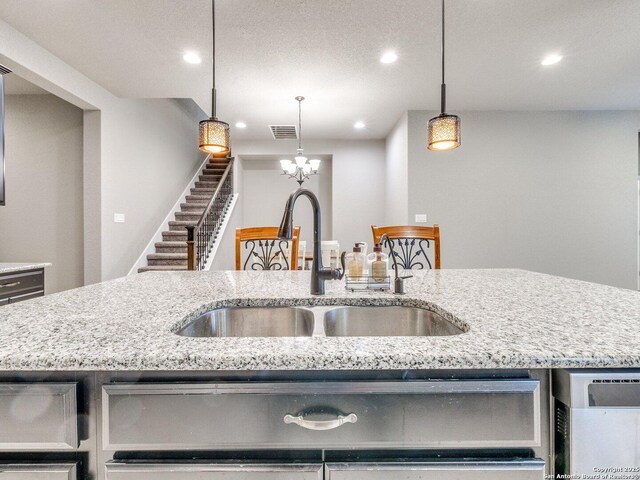 kitchen featuring decorative light fixtures, a center island with sink, light stone counters, and sink