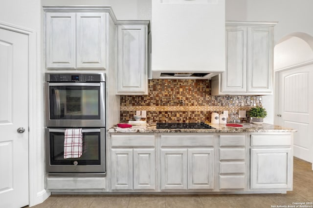 kitchen with light stone countertops, black gas cooktop, double oven, backsplash, and white cabinets