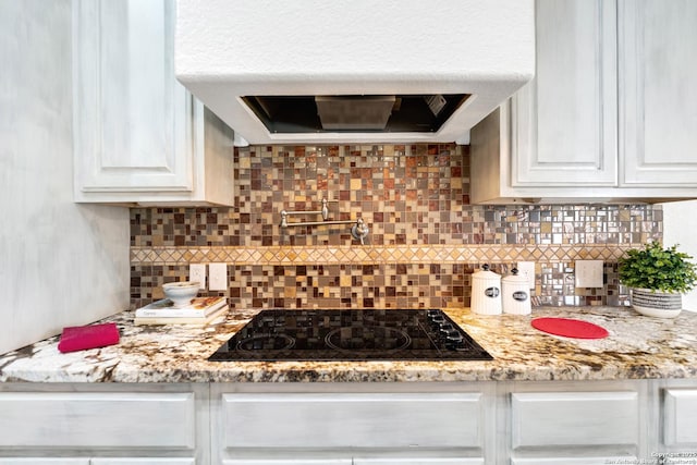 kitchen featuring decorative backsplash, light stone countertops, ventilation hood, black gas cooktop, and white cabinetry