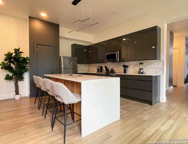 kitchen featuring sink, hanging light fixtures, tasteful backsplash, a center island with sink, and appliances with stainless steel finishes