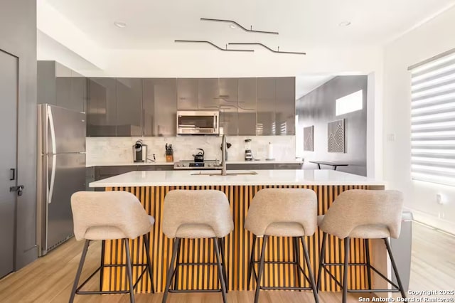 kitchen with a kitchen bar, stainless steel appliances, gray cabinets, and sink