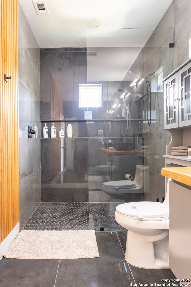 bathroom with vanity, tile patterned flooring, toilet, tile walls, and a tile shower