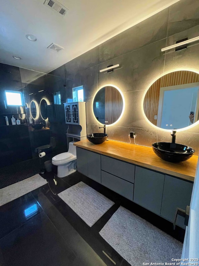 bathroom featuring a tile shower, vanity, toilet, and tile walls