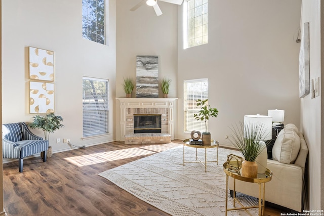 living room featuring ceiling fan, hardwood / wood-style floors, a towering ceiling, and a brick fireplace