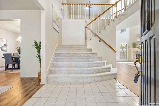 stairs with wood-type flooring, a high ceiling, and a tiled fireplace