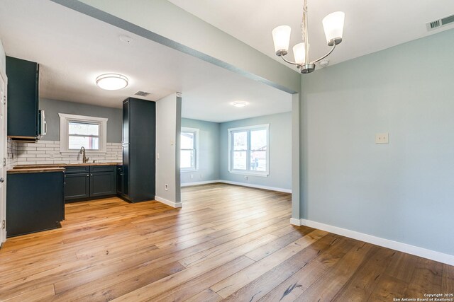 kitchen with decorative backsplash, light wood-type flooring, pendant lighting, an inviting chandelier, and butcher block counters