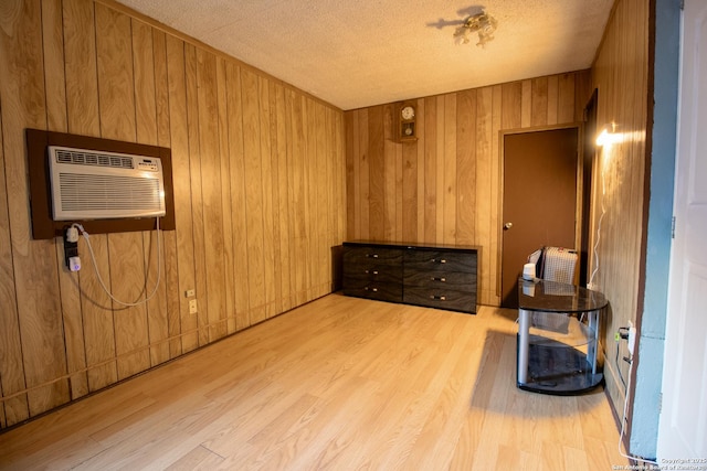 interior space featuring a textured ceiling, light hardwood / wood-style flooring, a wall mounted AC, and wooden walls