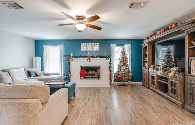 living room featuring a brick fireplace, a textured ceiling, light hardwood / wood-style flooring, and ceiling fan