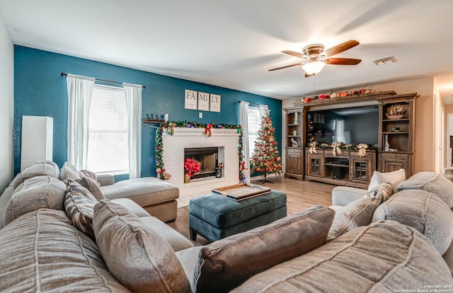 living room featuring ceiling fan, light hardwood / wood-style floors, and a fireplace