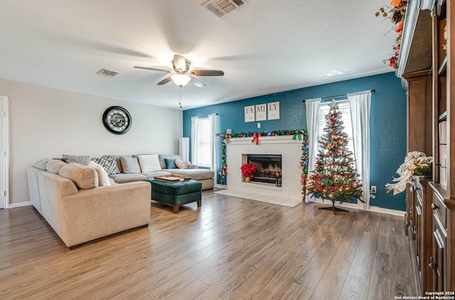 living room with ceiling fan, light hardwood / wood-style floors, a textured ceiling, and a brick fireplace