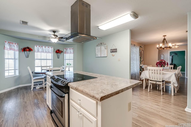 kitchen featuring a center island, ceiling fan with notable chandelier, electric stove, hanging light fixtures, and island range hood