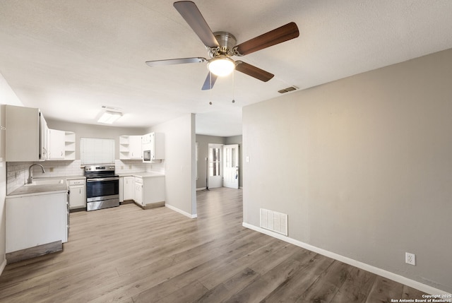 kitchen featuring backsplash, white cabinets, sink, light hardwood / wood-style flooring, and stainless steel range