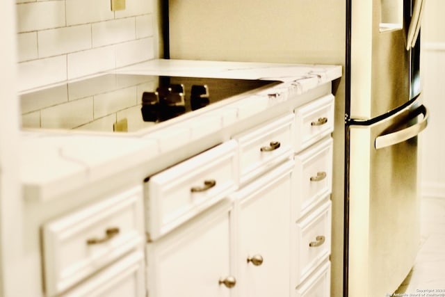 interior space featuring white cabinetry, black electric cooktop, stainless steel fridge, and light stone counters