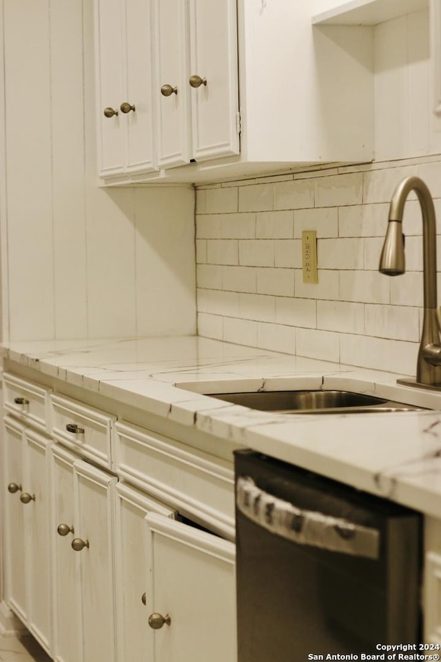 kitchen with sink, dishwasher, white cabinetry, backsplash, and light stone countertops