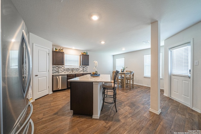 kitchen featuring backsplash, dark wood-type flooring, a kitchen breakfast bar, a kitchen island, and stainless steel appliances