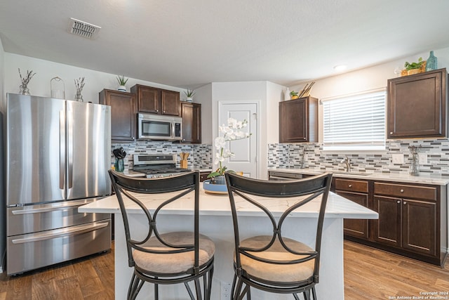 kitchen with a center island, a breakfast bar area, dark brown cabinets, appliances with stainless steel finishes, and light wood-type flooring