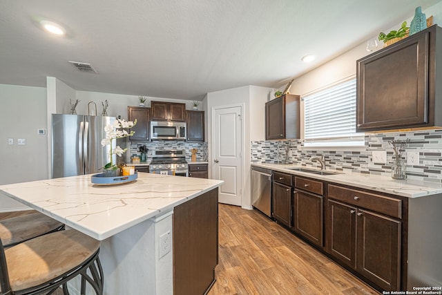 kitchen with dark brown cabinetry, sink, a center island, light hardwood / wood-style floors, and appliances with stainless steel finishes