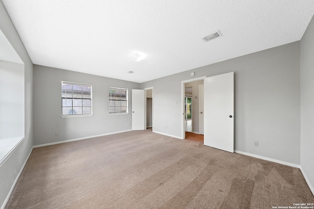 unfurnished bedroom featuring a textured ceiling, light colored carpet, and multiple windows