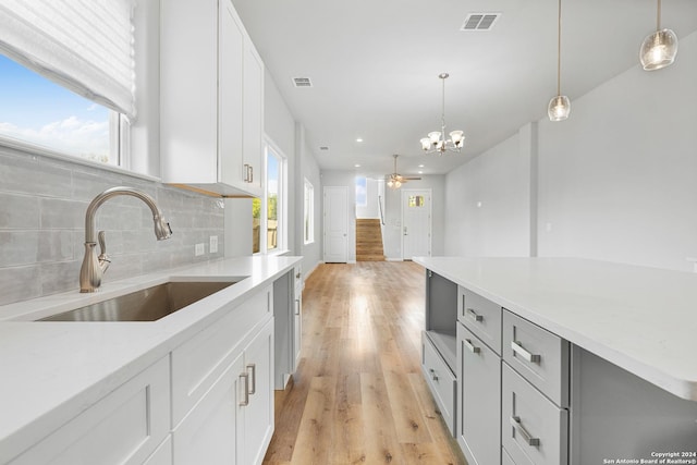 kitchen with decorative backsplash, ceiling fan with notable chandelier, sink, decorative light fixtures, and white cabinets