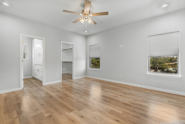 unfurnished bedroom featuring a spacious closet, ceiling fan, ensuite bathroom, light hardwood / wood-style floors, and a closet