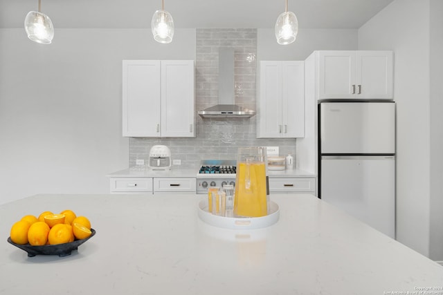 kitchen with light stone countertops, white fridge, white cabinetry, and wall chimney range hood