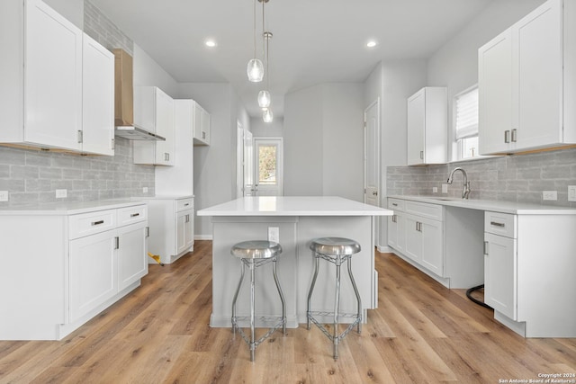 kitchen with tasteful backsplash, white cabinetry, light hardwood / wood-style flooring, and a kitchen island