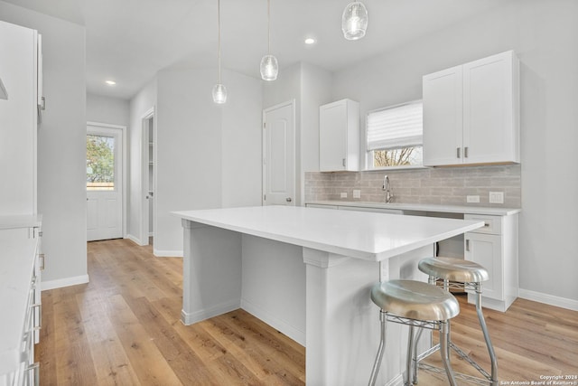 kitchen with white cabinetry, hanging light fixtures, a kitchen breakfast bar, tasteful backsplash, and a kitchen island