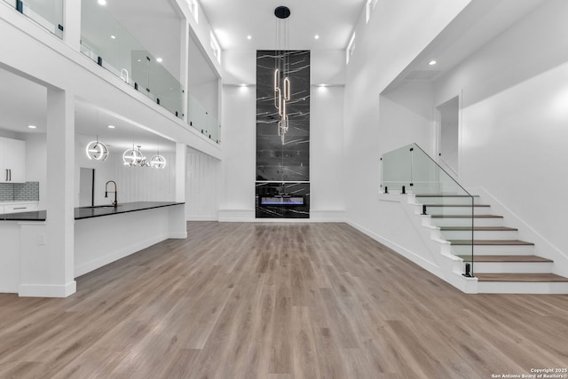 unfurnished living room with light hardwood / wood-style floors, sink, a high ceiling, and a chandelier