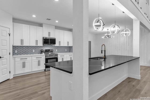 kitchen featuring white cabinetry, sink, stainless steel appliances, decorative light fixtures, and light wood-type flooring