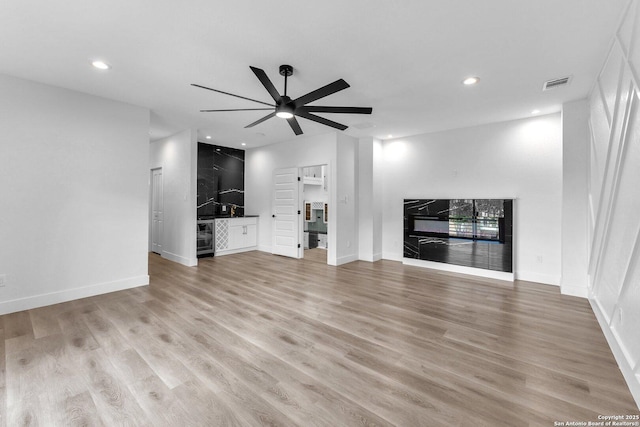 unfurnished living room with ceiling fan, light hardwood / wood-style flooring, and beverage cooler