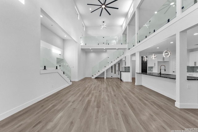 unfurnished living room with ceiling fan, sink, a high ceiling, and light wood-type flooring