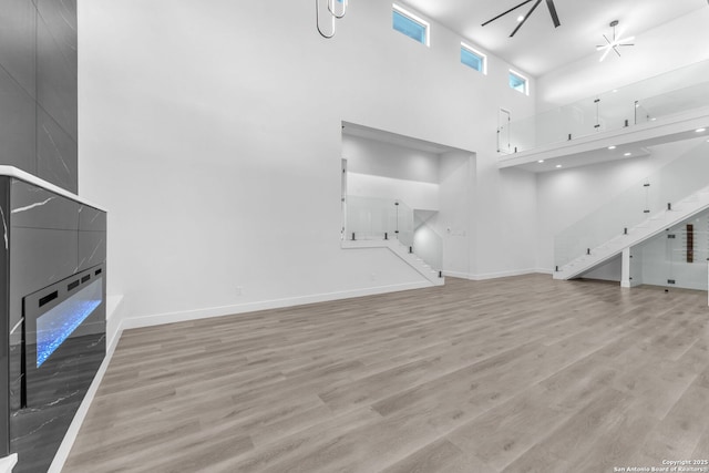 unfurnished living room featuring ceiling fan, a towering ceiling, and light wood-type flooring