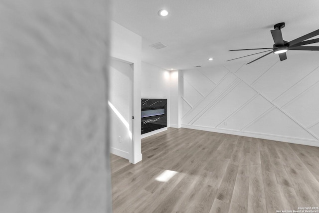 unfurnished living room featuring ceiling fan, a premium fireplace, a textured ceiling, and light hardwood / wood-style flooring