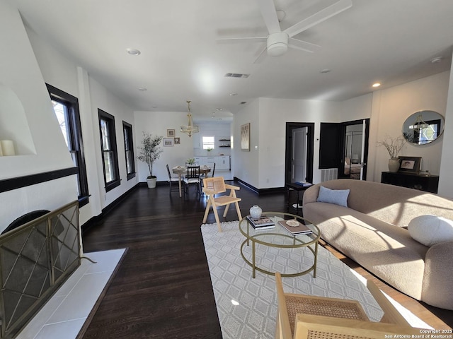 living room with ceiling fan with notable chandelier and dark hardwood / wood-style flooring