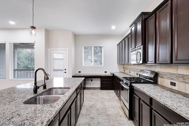 kitchen with light stone counters, stainless steel appliances, sink, decorative light fixtures, and plenty of natural light