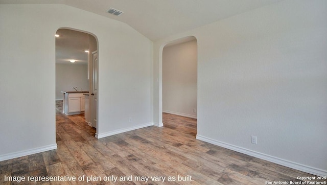 spare room featuring light wood-type flooring and vaulted ceiling