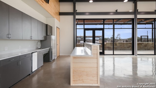 kitchen featuring stainless steel refrigerator, sink, a high ceiling, white dishwasher, and concrete flooring