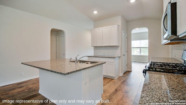 kitchen with light stone countertops, sink, vaulted ceiling, a center island with sink, and white cabinets