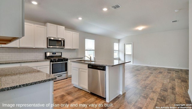 kitchen with appliances with stainless steel finishes, vaulted ceiling, a kitchen island with sink, sink, and white cabinets