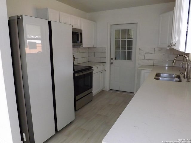 kitchen featuring light wood-type flooring, tasteful backsplash, stainless steel appliances, sink, and white cabinetry