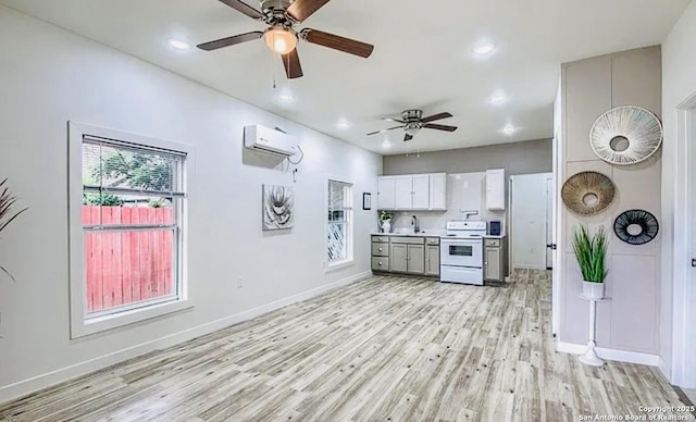 kitchen with a wall mounted air conditioner, sink, electric stove, light hardwood / wood-style floors, and white cabinetry