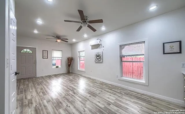 empty room with a wall mounted air conditioner, ceiling fan, and light wood-type flooring