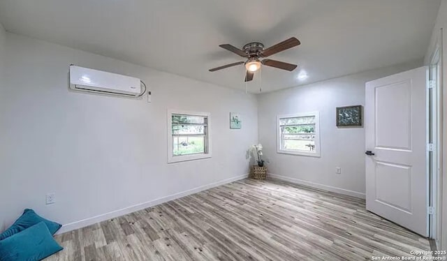 empty room featuring an AC wall unit, ceiling fan, and light wood-type flooring